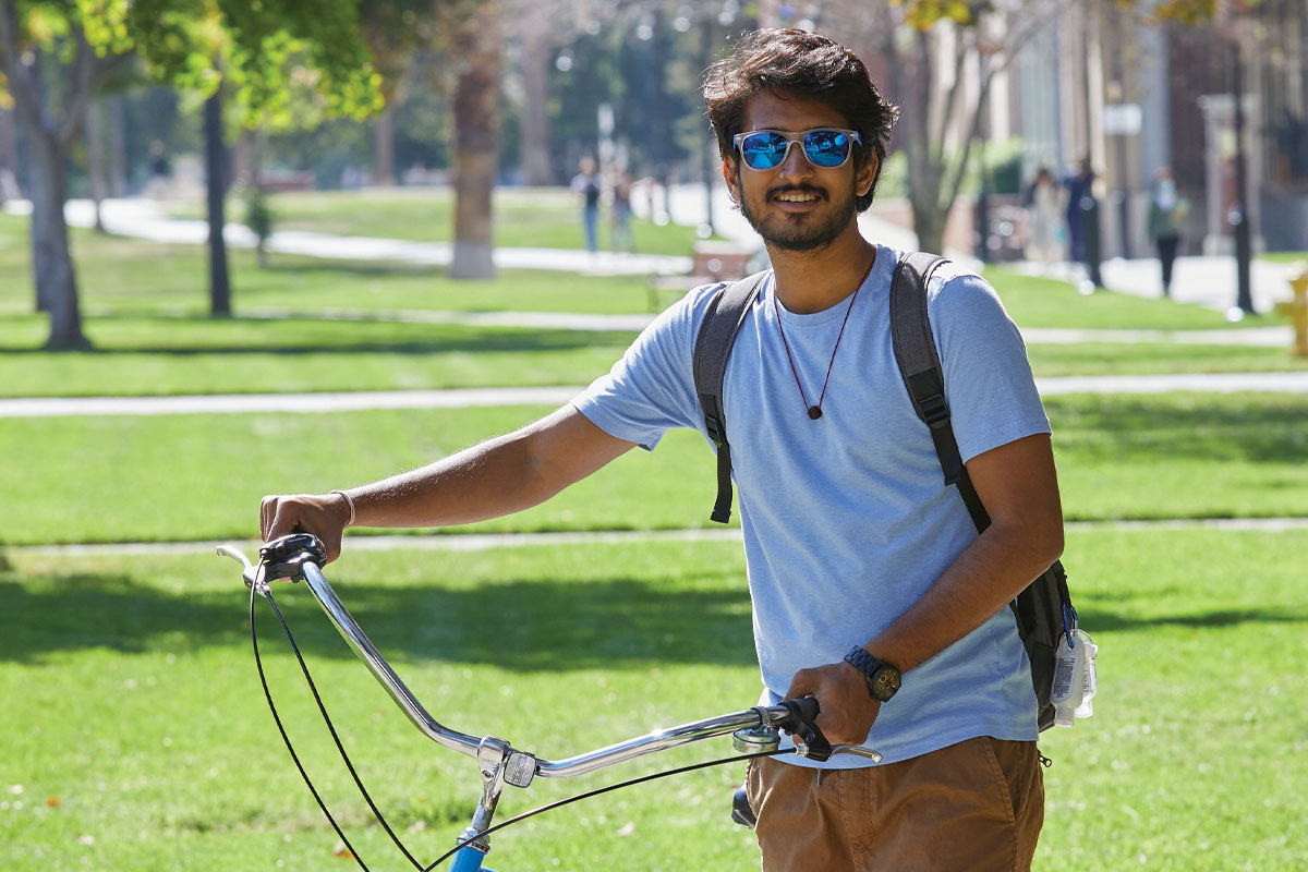 Student in sunglasses walking his bicycle