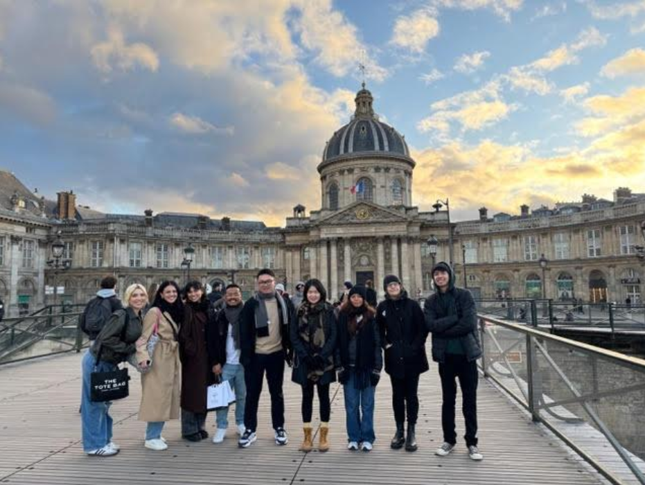 A group of people stands on a bridge, with a large building visible in the background.