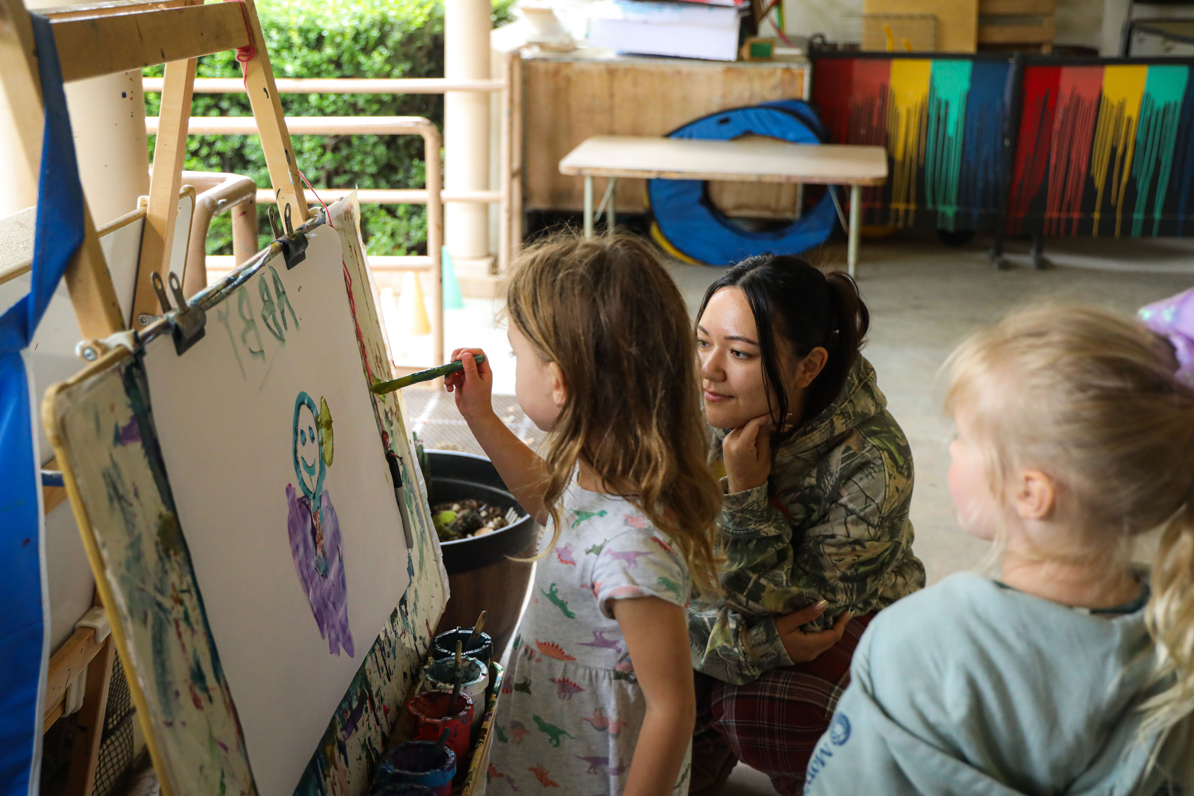 Child painting and another child and student teacher observing