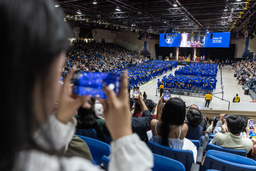 Guest taking a photo of a commencement ceremony inside an arena.