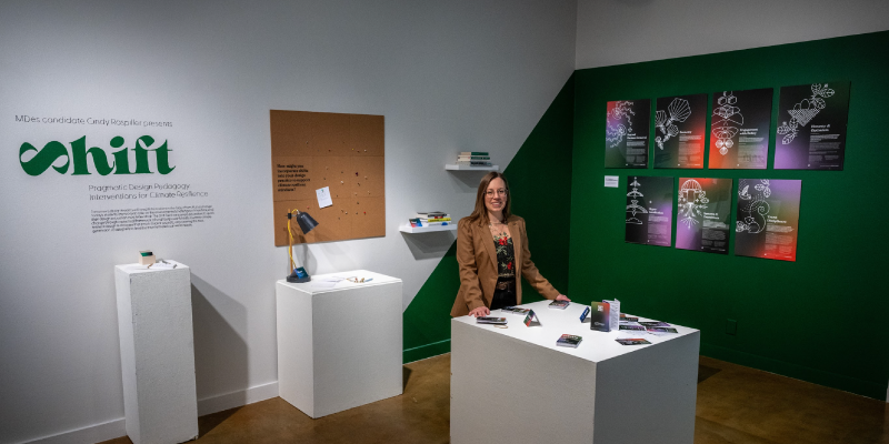 Designer Cindy Raspiller posing in front of gallery exhibition.