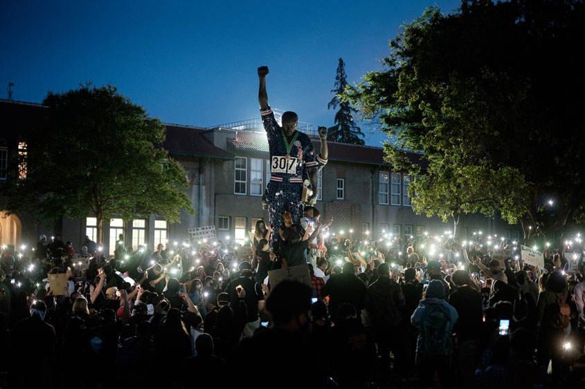Students Peacefully protesting at SJSU Smith and Carlos Olympic Statue at night while holding up phones creating a glowing effect