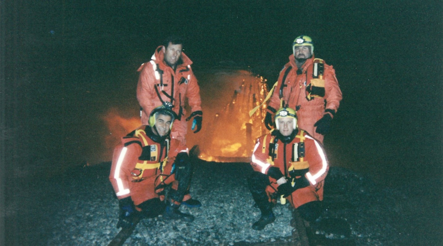 four firefighters pose in front of fire at night