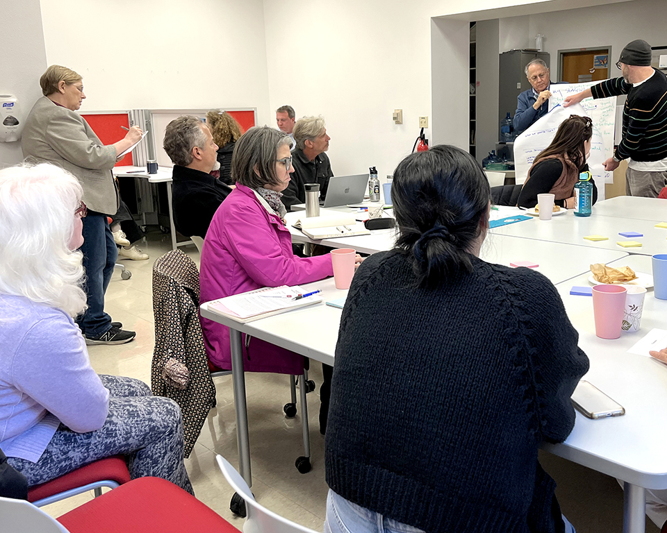 faculty and staff are gathered around a table and focused on two presenter in front of the room, they are discussing future curriculum