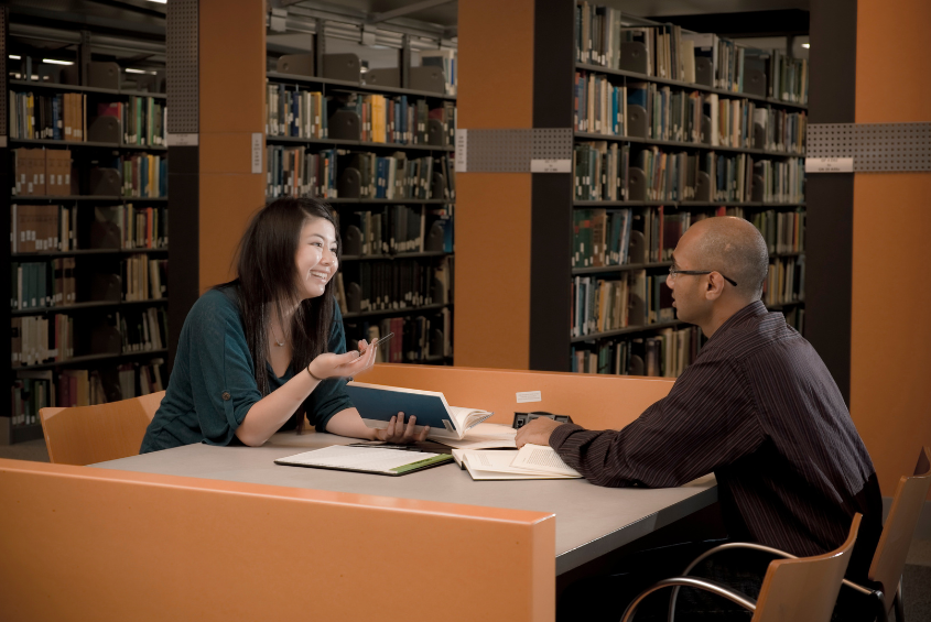 Two people talking in a library.