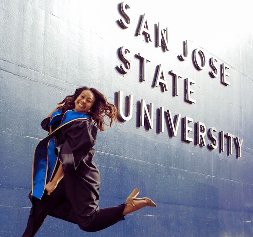Graduate student jumping joyfully in front of the San José State University sign.